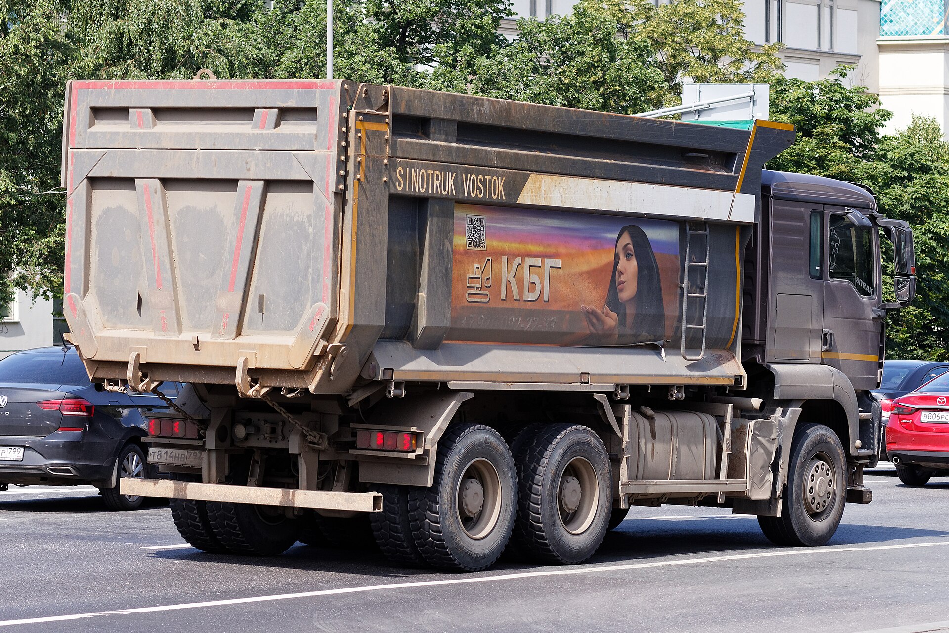 Серый самосвал SITRAK C7H на городской дороге, вид сбоку и спереди